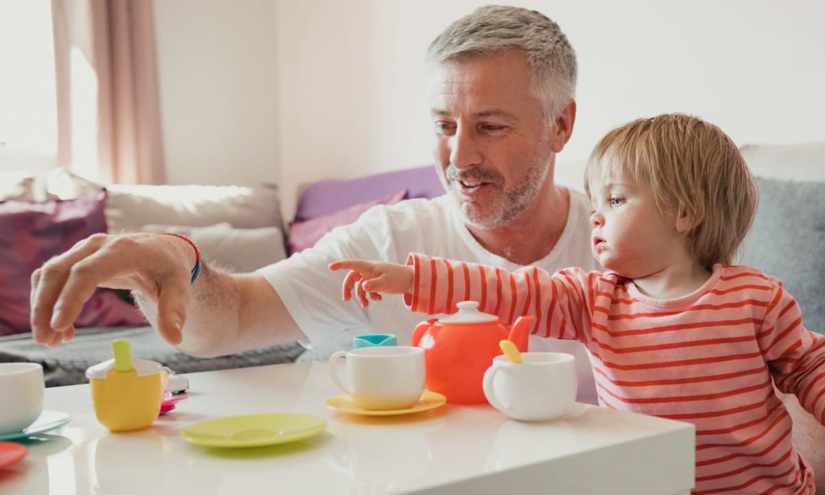 A toddler and father playing together with a plastic tea set
