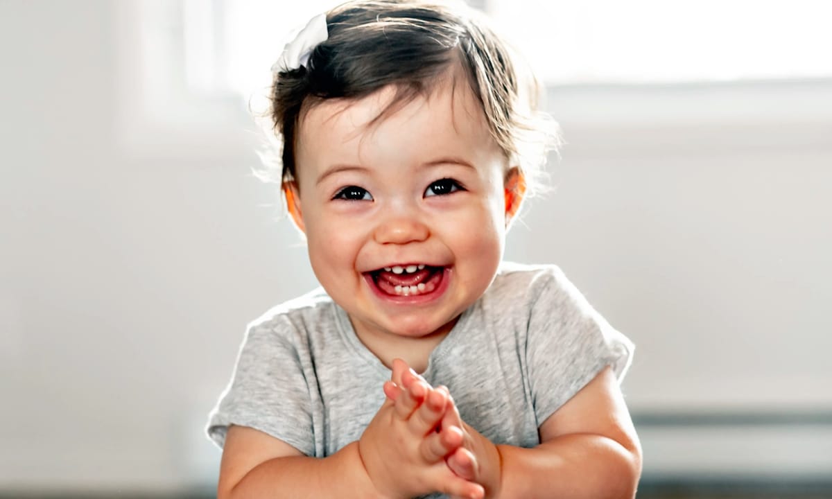 A nine month old baby clapping and smiling