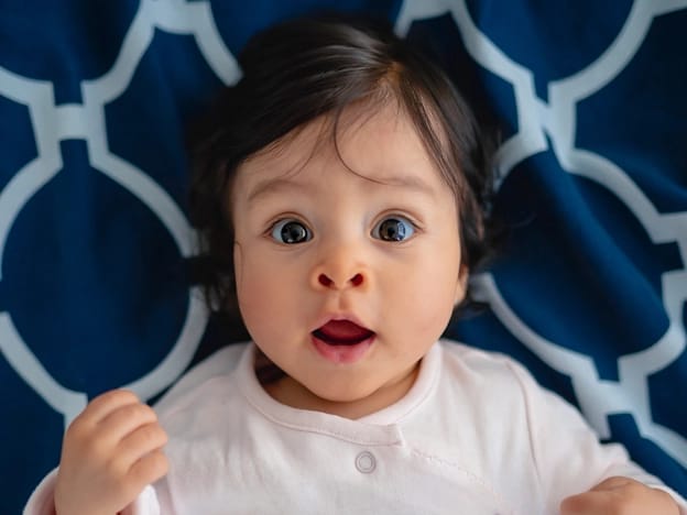 Wide eyed baby girl lying on a patterned blue sheet