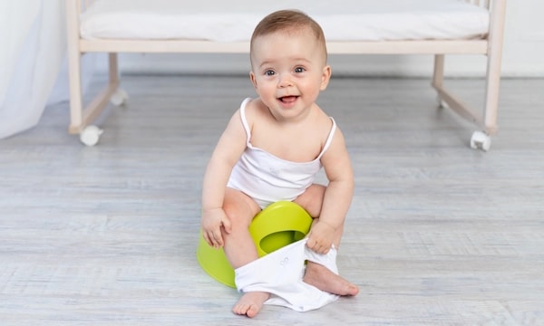 Smiley baby sitting on a green potty doing elimination communication
