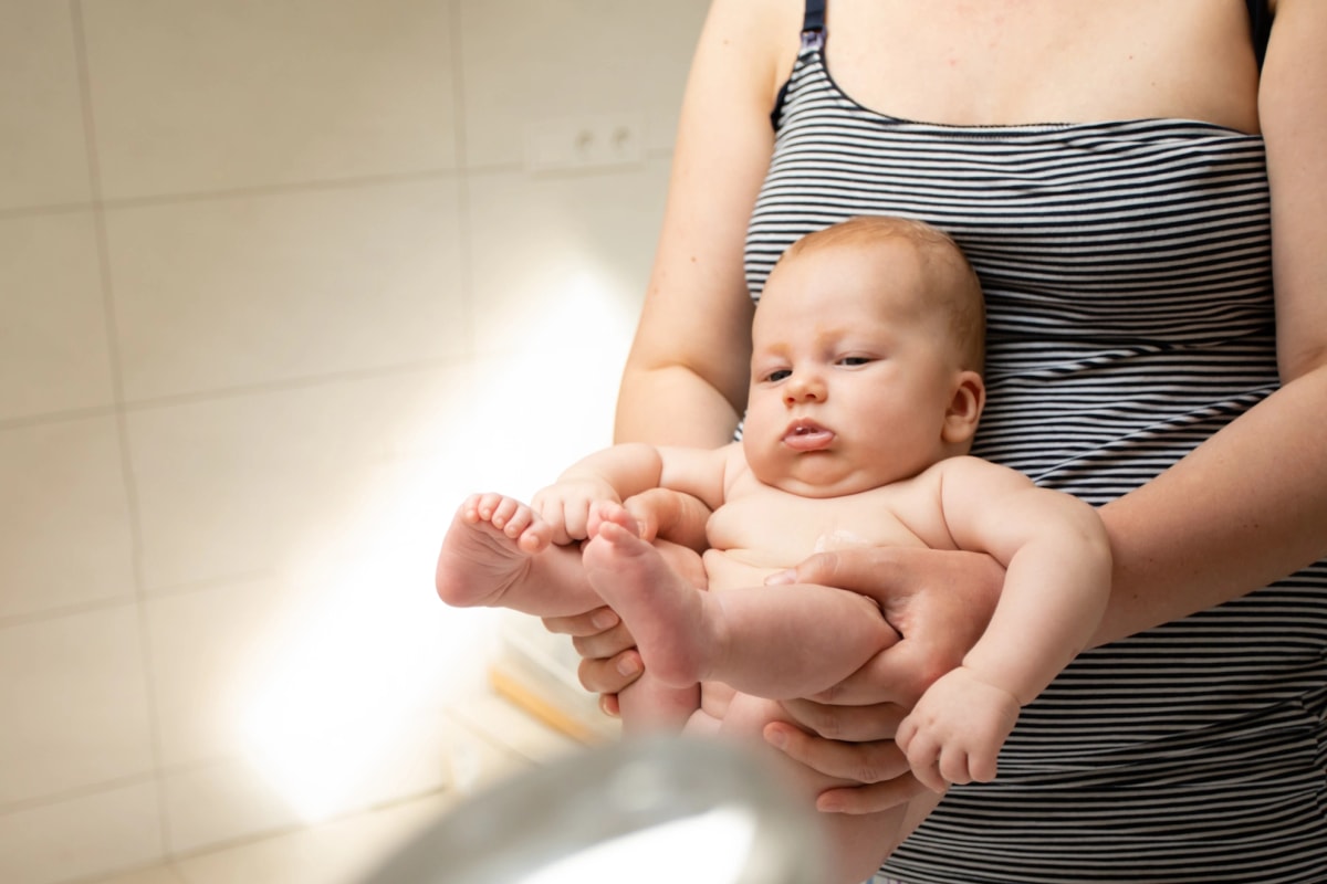 Elimination Communication with a newborn, mother holding a newborn over a sink to pee