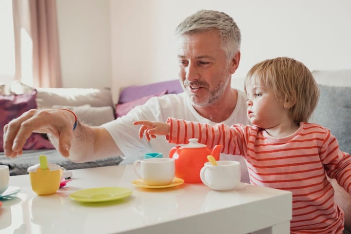 A toddler and father playing together with a plastic tea set